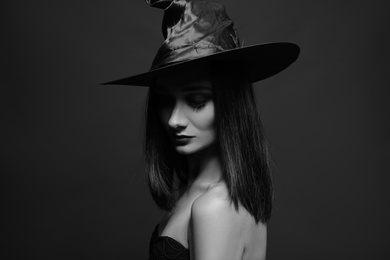 Photo of Mysterious witch wearing hat on dark background. Black and white effect