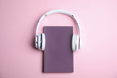 Photo of Book and modern headphones on pink background, top view