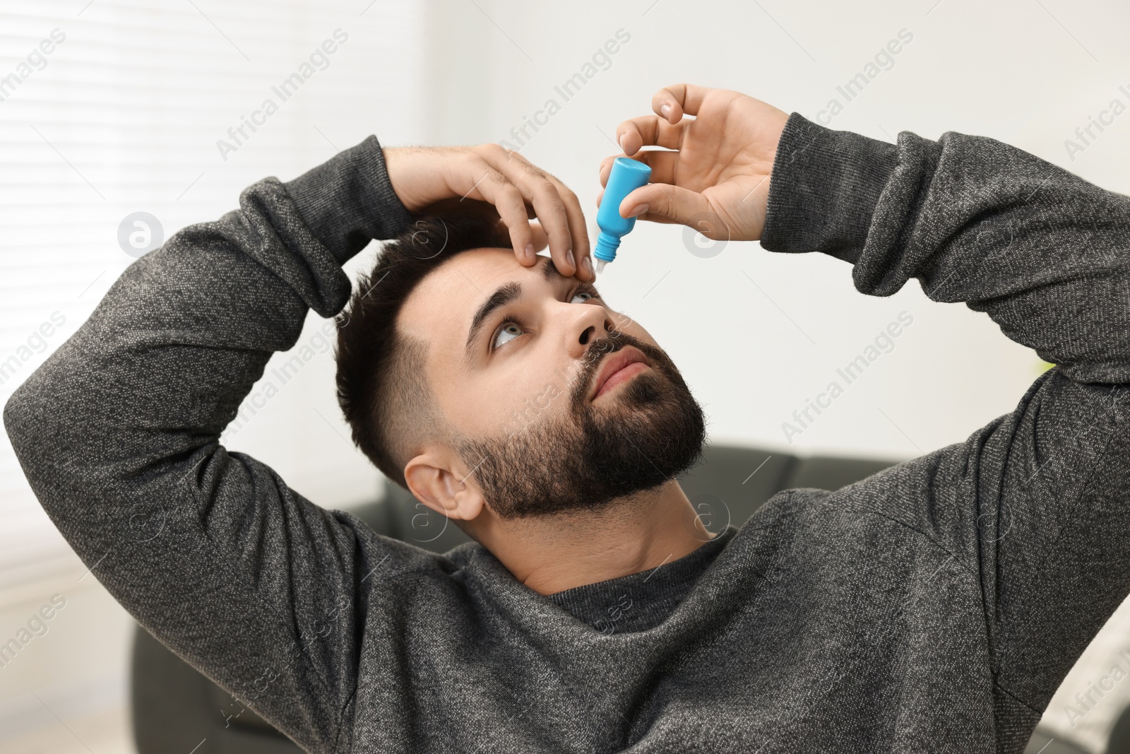 Photo of Young man applying medical eye drops indoors