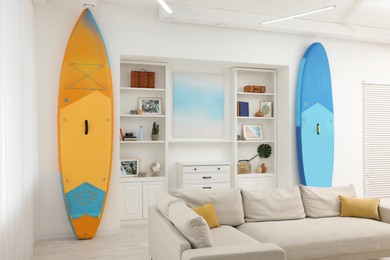 SUP boards, shelving unit with different decor elements and stylish sofa in room. Interior design