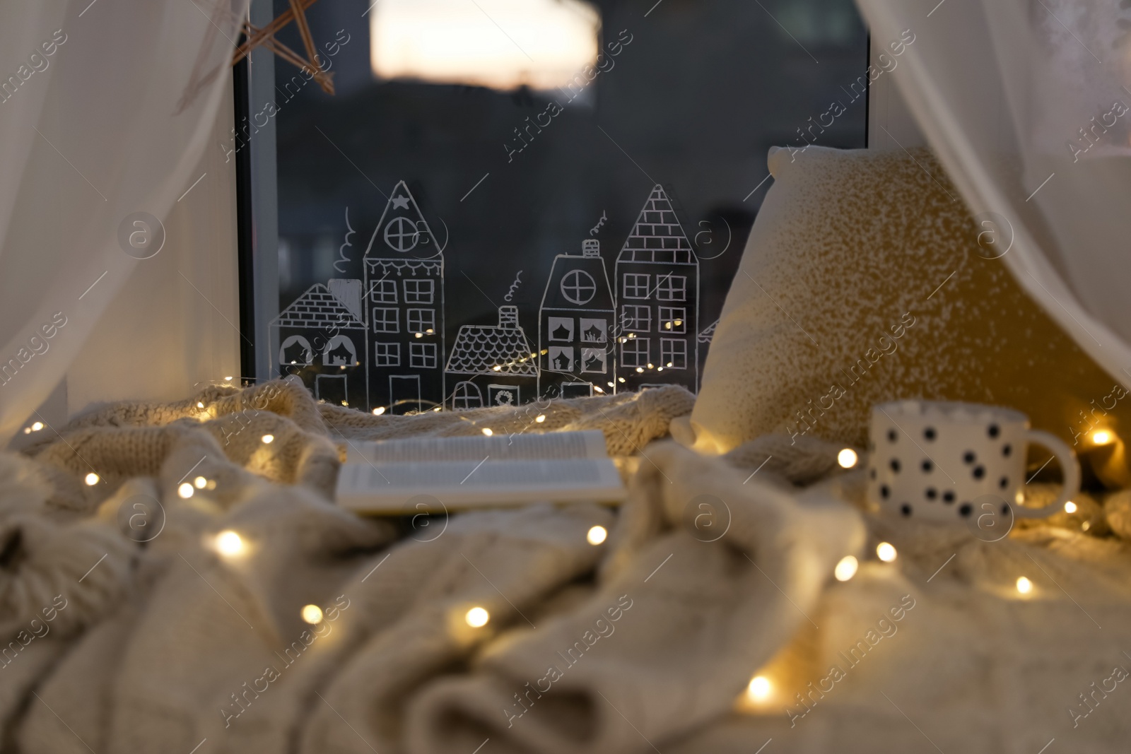 Photo of Open book and cup of hot drink on plaid near window with beautiful drawing at home. Christmas decor