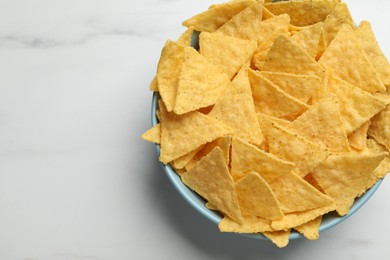 Photo of Tortilla chips (nachos) in bowl on white table, top view. Space for text