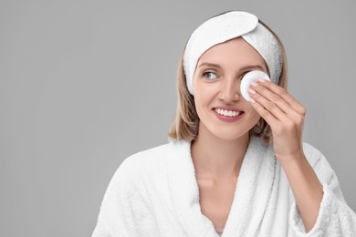 Photo of Young woman cleaning face with cotton pad on light grey background. Space for text