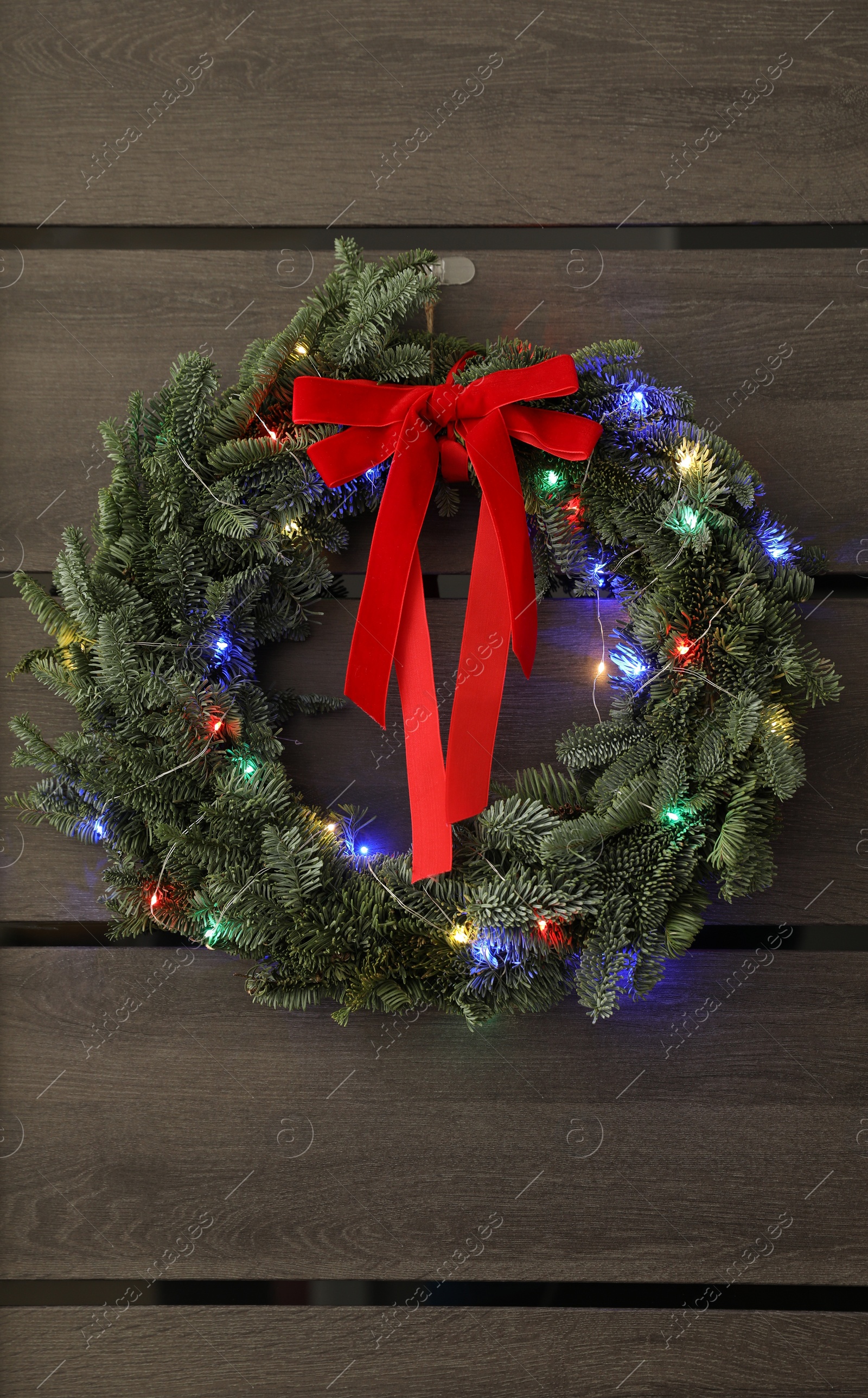 Photo of Beautiful Christmas wreath with red bow and festive lights hanging on door