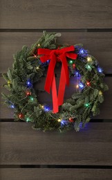 Photo of Beautiful Christmas wreath with red bow and festive lights hanging on door