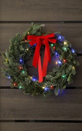 Beautiful Christmas wreath with red bow and festive lights hanging on door