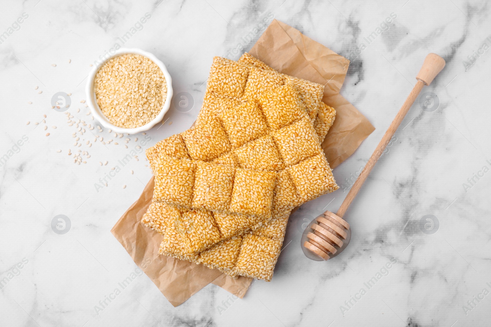 Photo of Delicious sweet kozinaki bars, sesame seeds and wooden dipper on white marble table, flat lay