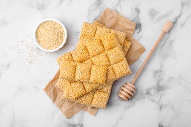 Photo of Delicious sweet kozinaki bars, sesame seeds and wooden dipper on white marble table, flat lay