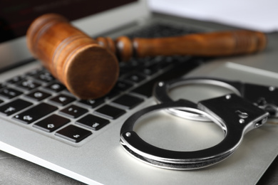 Photo of Laptop, gavel and handcuffs on table, closeup. Cyber crime