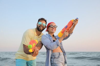 Photo of Happy couple with water guns near sea at sunset