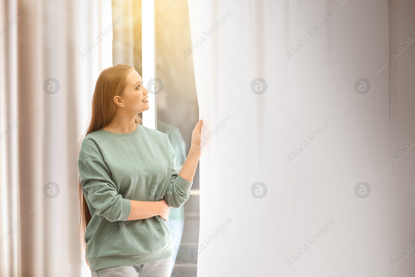 Image of Beautiful young woman looking out of window at home