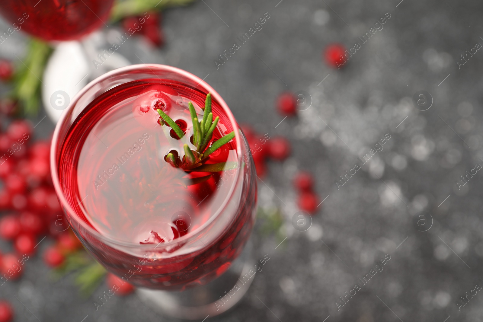 Photo of Tasty cranberry cocktail with rosemary in glass on gray table, above view. Space for text