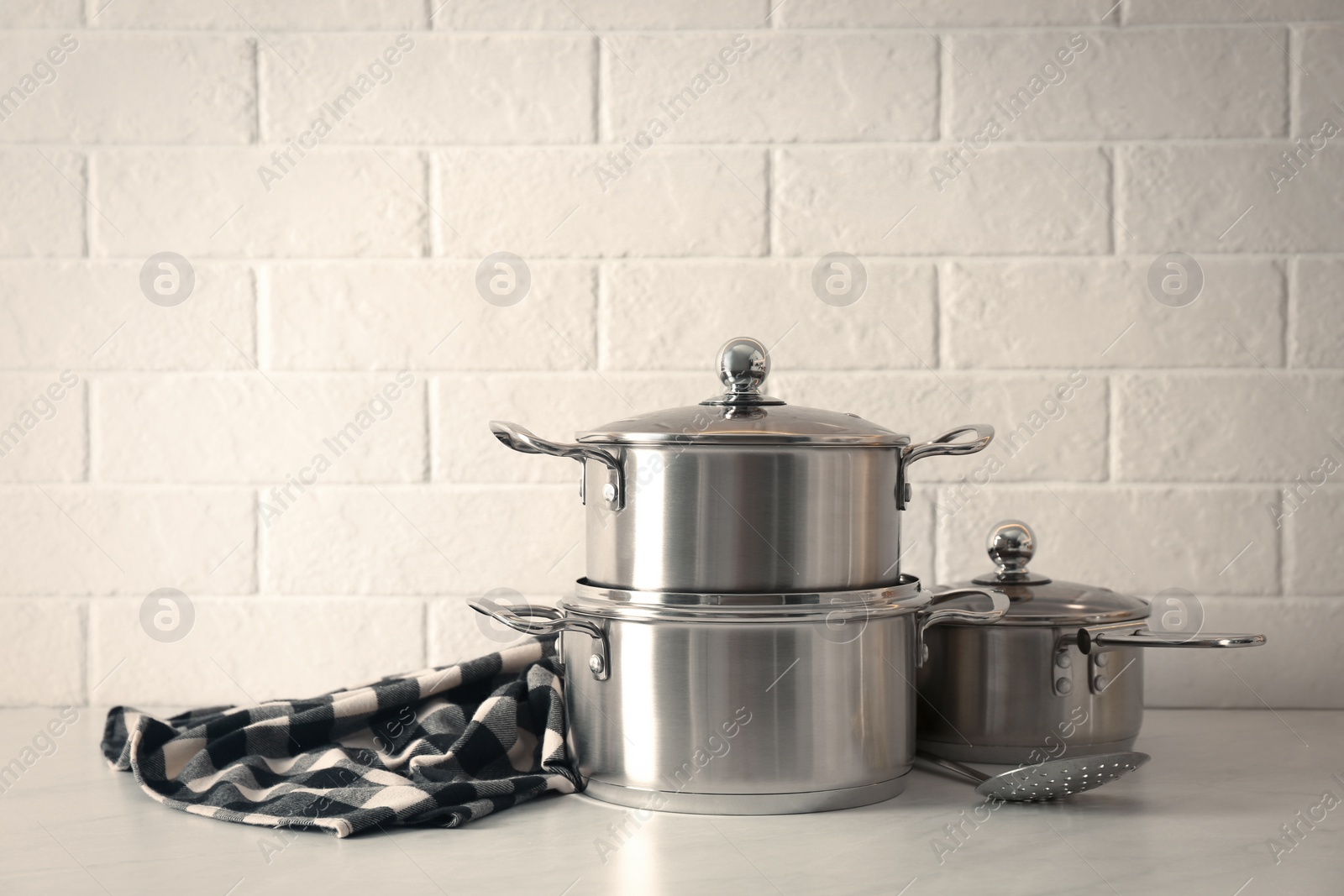 Photo of Set of stainless steel cookware on table near white brick wall