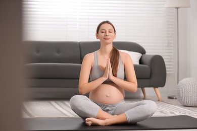 Pregnant woman meditating on yoga mat at home