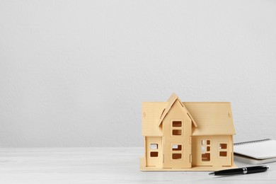 Photo of Mortgage concept. House model, notebook and pen on white wooden table, space for text