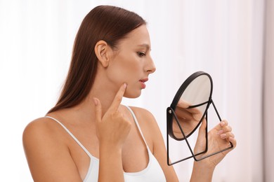 Woman with skin problem looking at mirror indoors