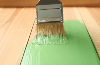 Applying green paint onto wooden surface, closeup