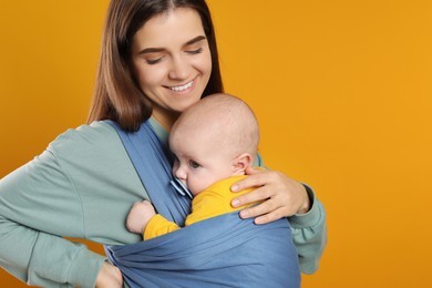 Photo of Mother holding her child in sling (baby carrier) on orange background