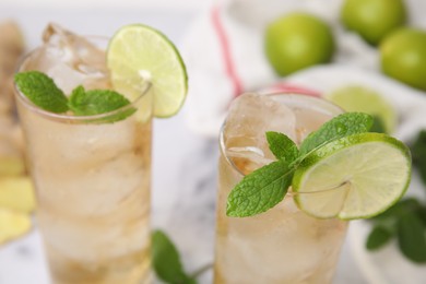 Photo of Glasses of tasty ginger ale with ice cubes, lime slices and mint on blurred background, closeup