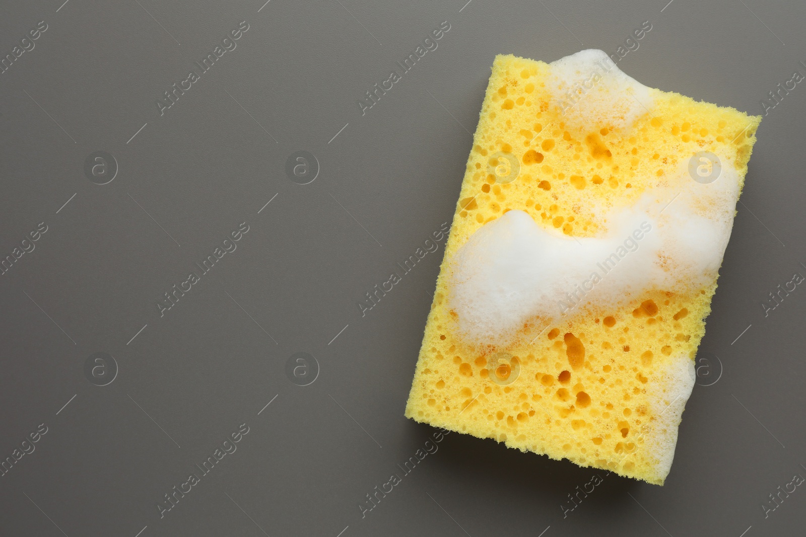 Photo of Yellow sponge with foam on grey background, top view. Space for text