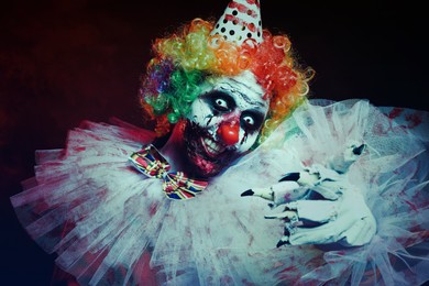 Photo of Terrifying clown on dark background. Halloween party costume