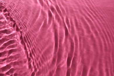 Photo of Rippled surface of clear water on bright pink background, top view