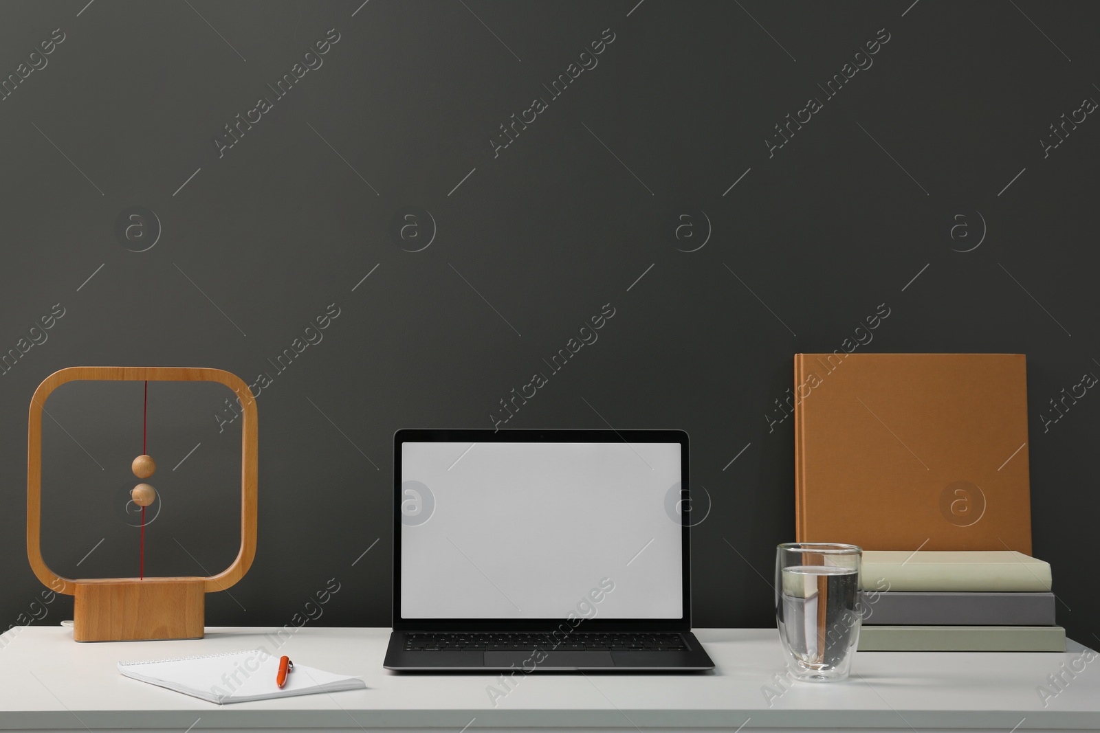 Photo of Stylish workplace with laptop, glass of water, books and decor on white table near grey wall