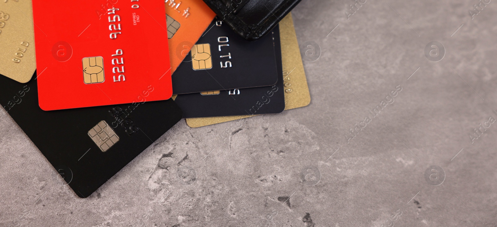 Photo of Pile of different credit cards on grey table, top view. Space for text