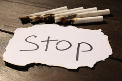 Burnt cigarettes and word Stop written on paper on wooden table, closeup. No smoking concept