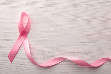 Pink ribbon on wooden background, top view with space for text. Breast cancer awareness concept
