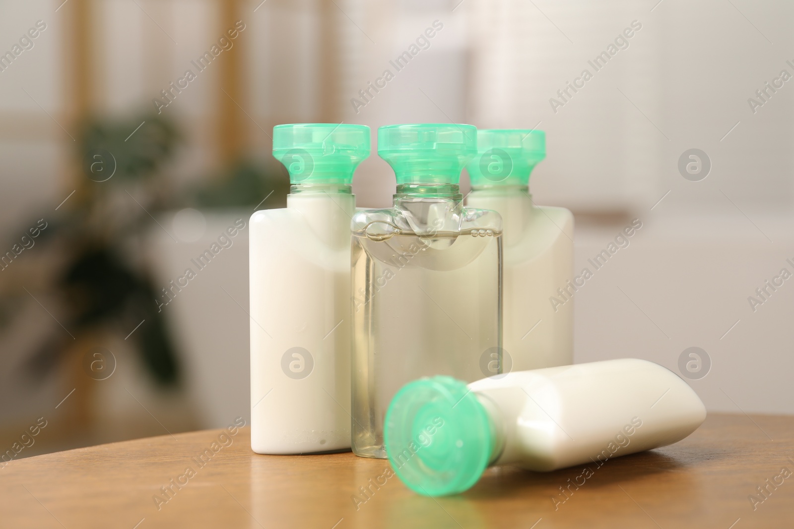 Photo of Mini bottles of cosmetic products and green branch on wooden table against blurred background, closeup