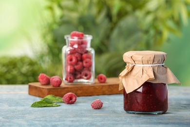 Photo of Jar with raspberry jam on table against blurred background