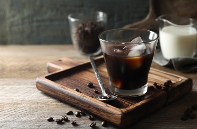 Glass of delicious iced coffee and beans on wooden table, space for text