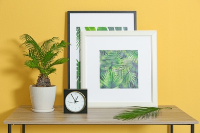 Photo of Pot with Sago palm tree and pictures of tropical leaves on table in room interior