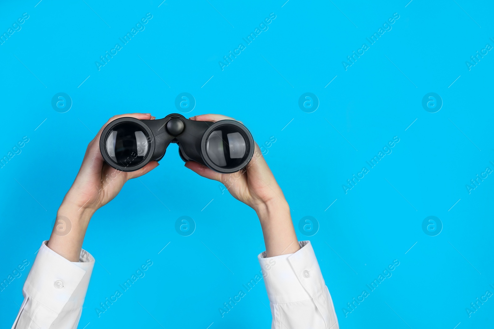 Photo of Woman holding modern binoculars on light blue background, closeup. Space for text