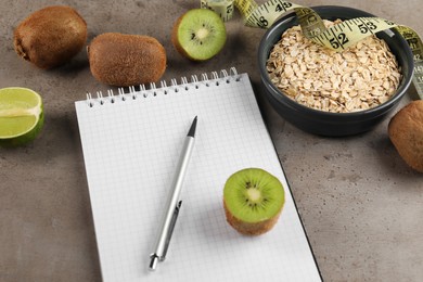 Photo of Healthy diet. Notebook, measuring tape, pen and products on grey table