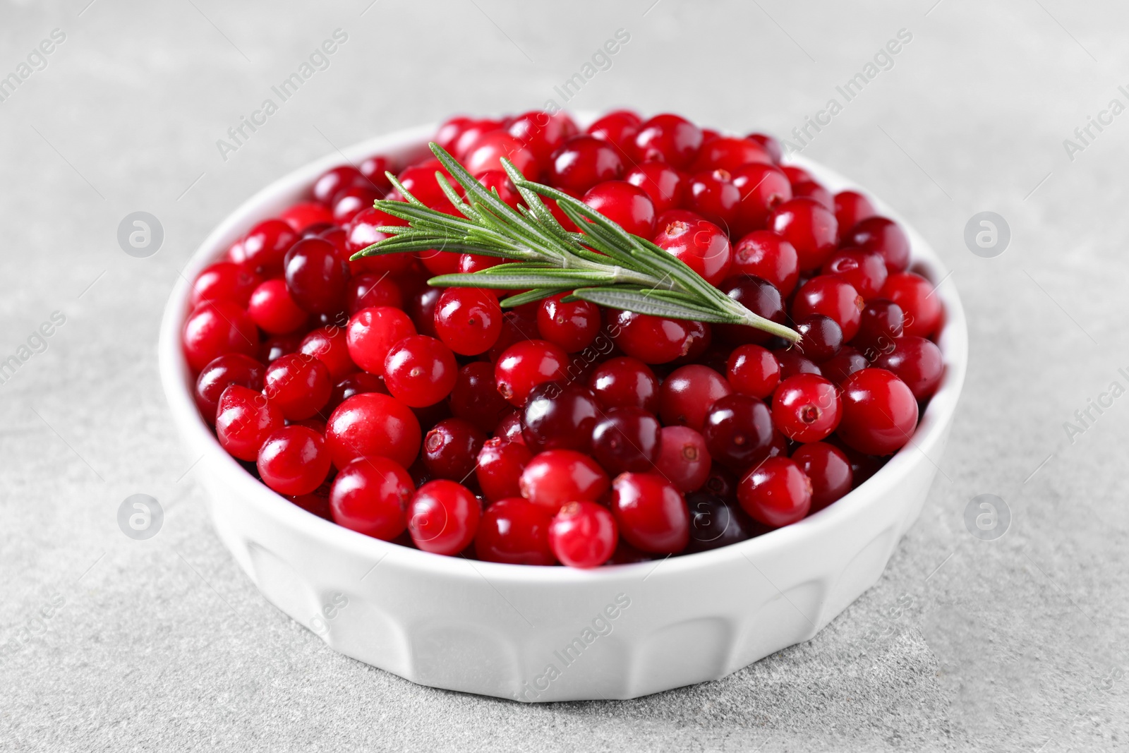 Photo of Fresh ripe cranberries and rosemary in bowl on grey table, closeup