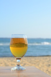 Photo of Glass of cold beer on wooden table at beach