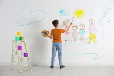 Image of Little child drawing family on white wall indoors