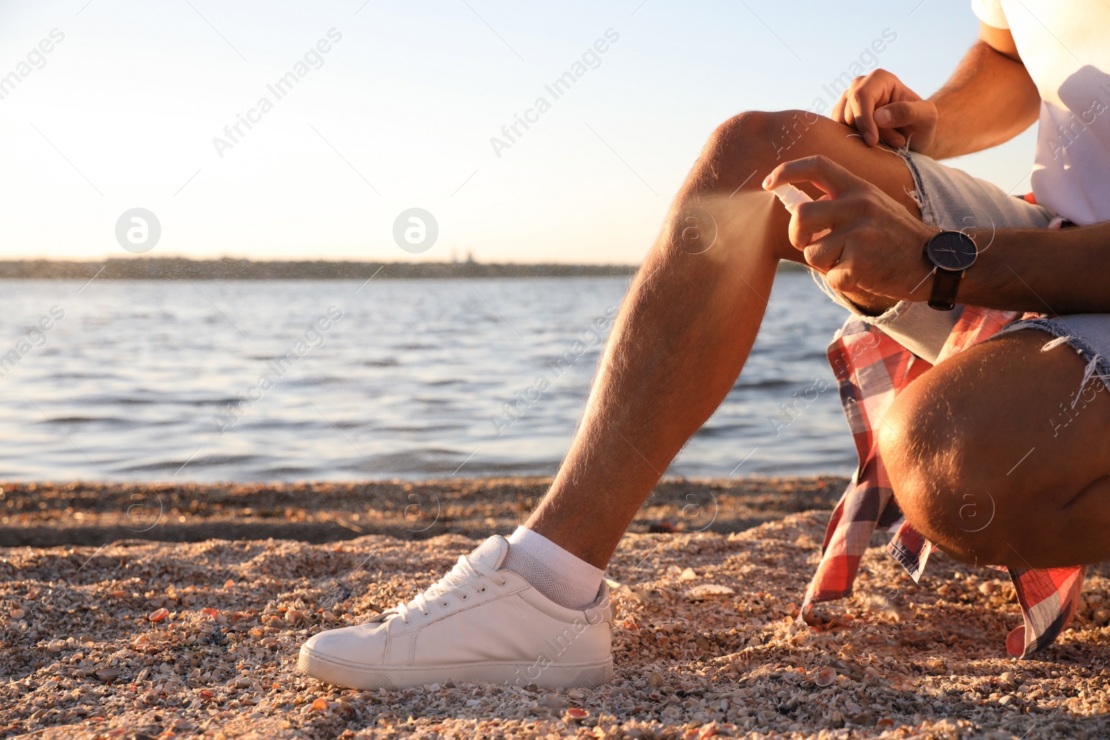 Photo of Man using insect repellent near sea on sunny day, closeup