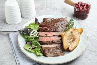 Photo of Delicious roasted beef meat, caramelized pear and greens served on light textured table