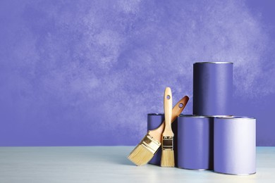 Cans with paint and brushes on table against violet background. Space for text