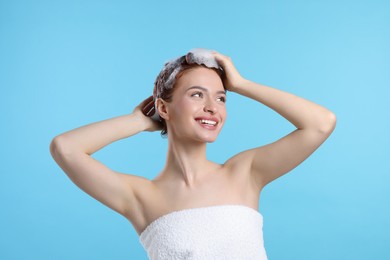 Happy young woman washing her hair with shampoo on light blue background