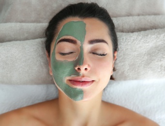 Photo of Pretty woman with clay mask on her face in spa salon, above view