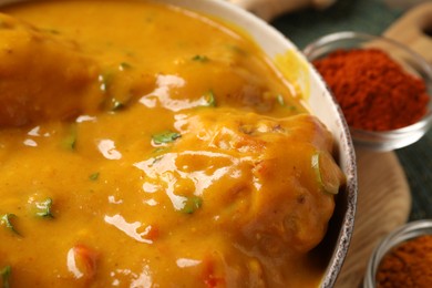 Photo of Tasty chicken curry and spices on wooden board, closeup