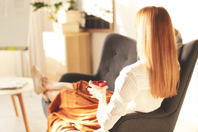 Young woman with cup of drink relaxing on couch at workplace