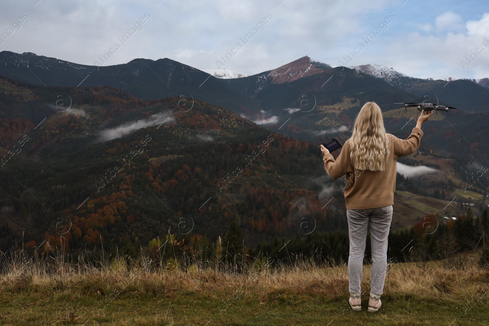 Photo of Young woman with modern drone in mountains, back view. Space for text