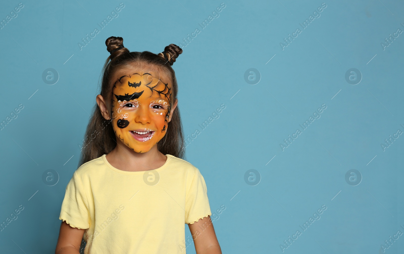 Photo of Cute little girl with face painting on blue background. Space for text
