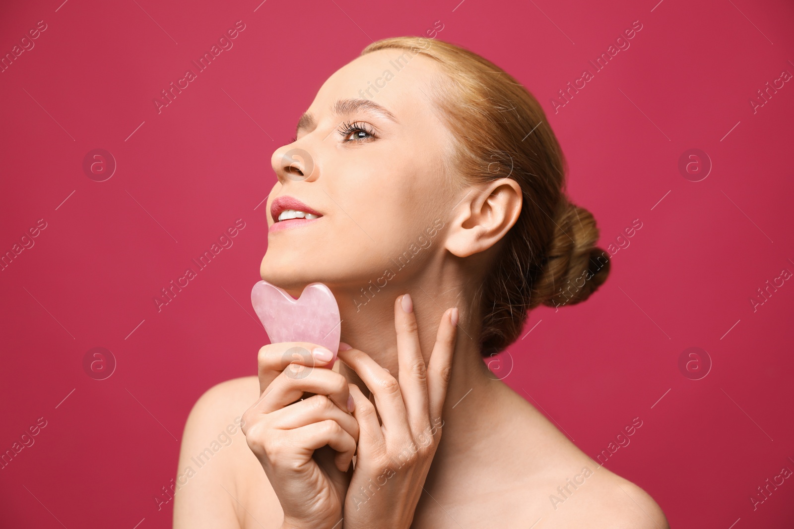 Photo of Beautiful young woman doing facial massage with gua sha tool on pink background