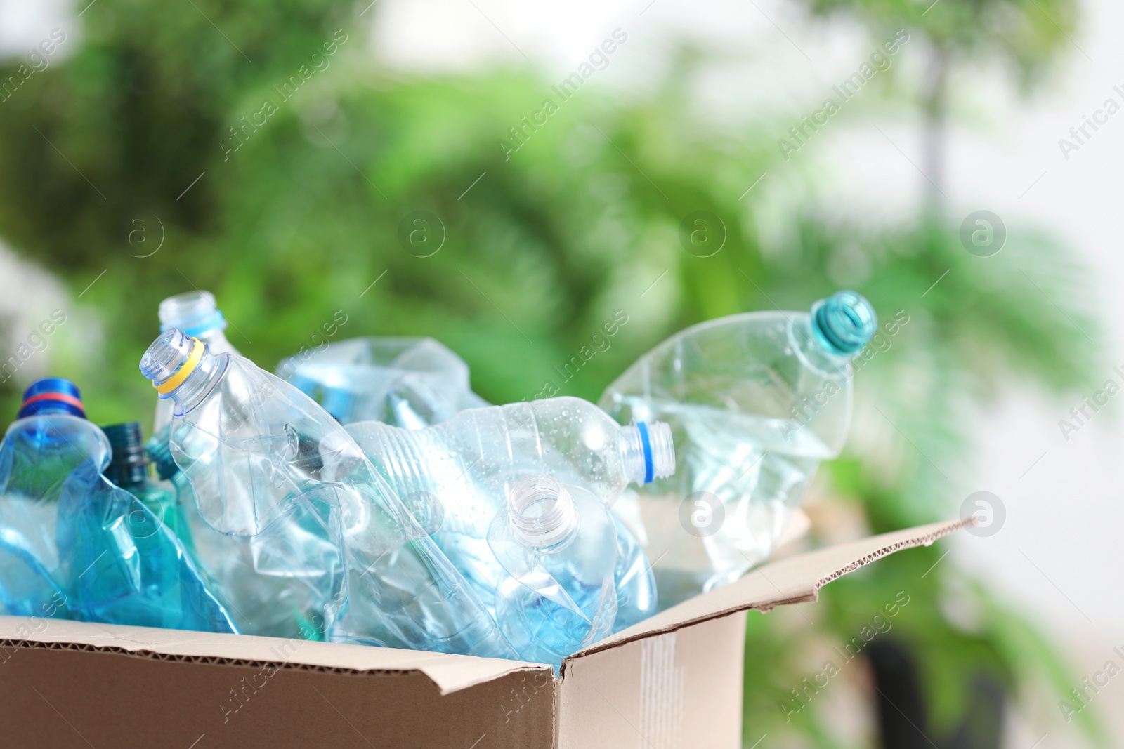 Photo of Cardboard box with used plastic bottles on blurred background. Recycling problem